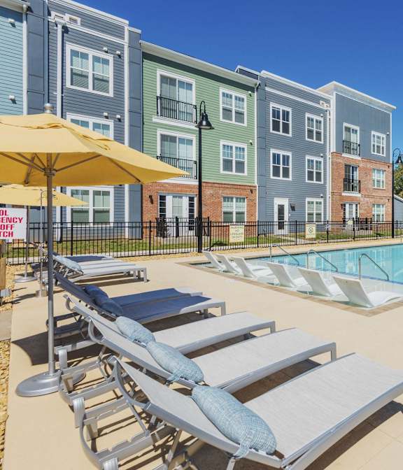 A pool area with sun loungers and a pool in front of apartment buildings.
