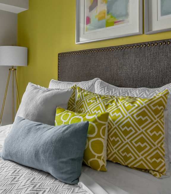 A bed with a grey headboard and yellow and grey pillows.