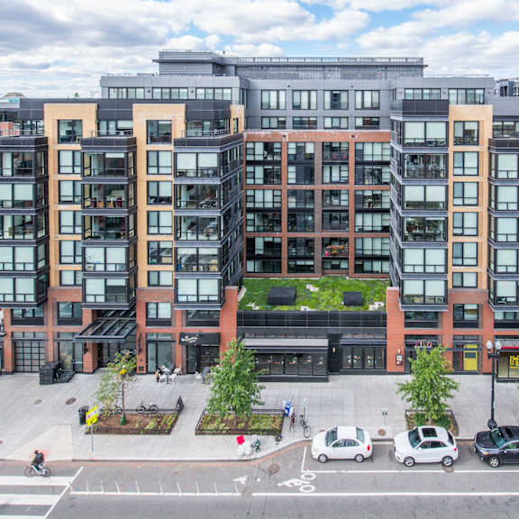 A modern apartment building with a green roof and a parking lot in front.
