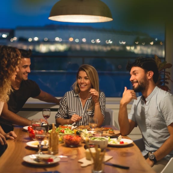Group of people sitting around a table eating food and drinking wine