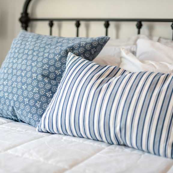 A bed with a white comforter and blue and white striped pillows.