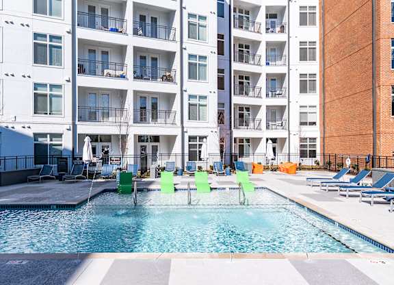 a swimming pool with green chairs in front of an apartment building