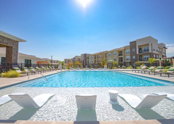a swimming pool with chairs and an apartment building in the background