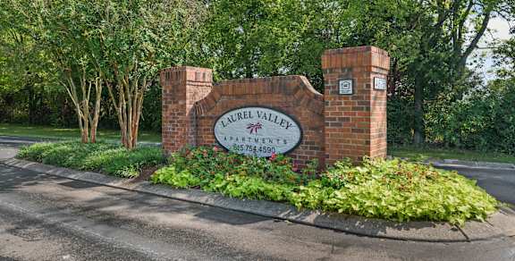 A sign for Laurel Valley Apartments stands in front of a green tree.