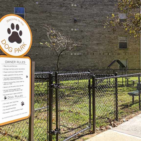 A sign for a dog park is posted on a fence.