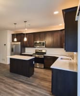 an open kitchen and living room with wood flooring and dark cabinets