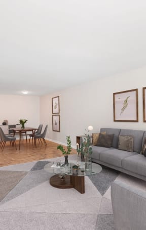 A living room with a grey couch, a coffee table, a dining table, and a television at The Alpine Apartments, Kettering, Ohio