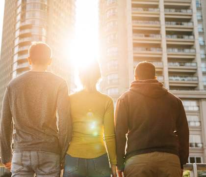 Three people are standing on a balcony looking at a tall building.