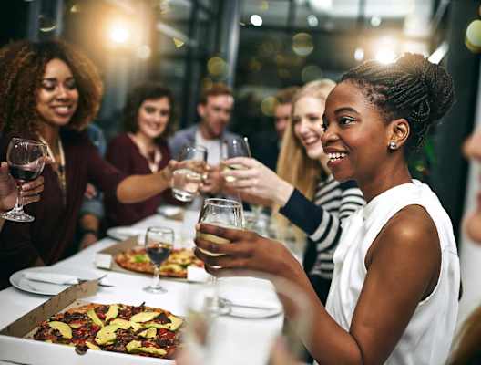 a group of people sitting around a table eating pizza and drinking wine