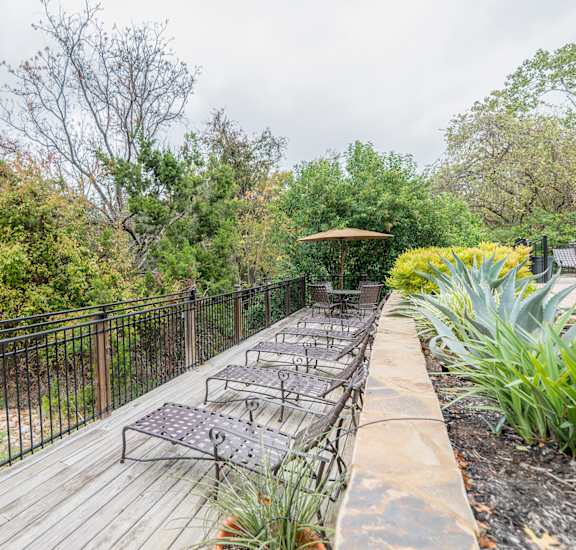 a patio with benches and a fence and trees at High Oaks, Austin, 78759