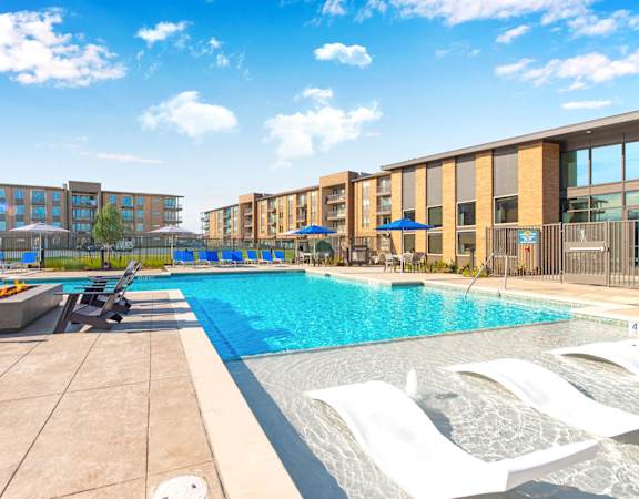 A swimming pool with sun loungers and apartment buildings in the background.