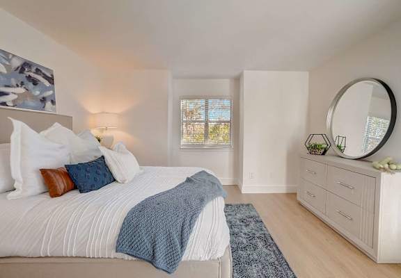 A bedroom with a large bed and a round mirror on the dresser.