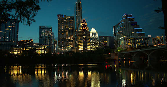 A city skyline at night with buildings reflecting in the water.