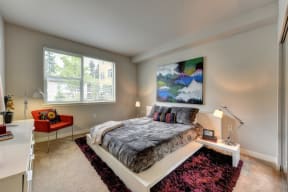 Bedroom with Large Window, Carpet through out but has a burgundy accent rug and abstract painting on wall and Low Elevated Mattress