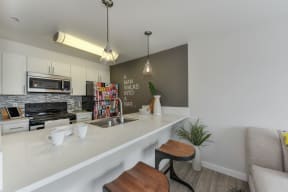 Kitchen Bar Seating with White Countertop, Mugs and Bowls, Sink and "A Man Walks Into a Bar" Painted on the Wall, 