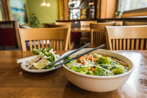 a bowl of pho and a plate of salad sit on a table in a restaurant