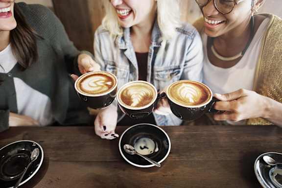 Four people are sitting at a table with cups of coffee in front of them.