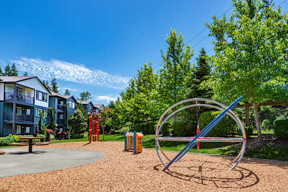 A playground with a large metal ring structure in the foreground and apartment buildings in the background.