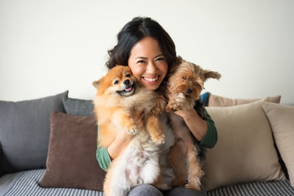 Woman Smiling and Holding Two Small Dogs in Both Arms
