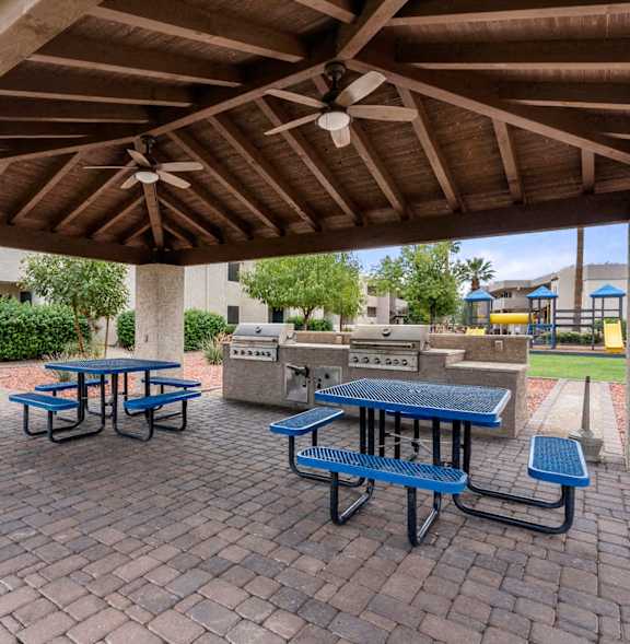 A BBQ grill is in the foreground of a residential area with palm trees.