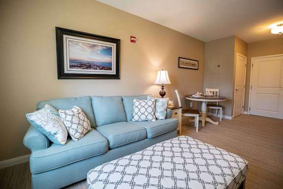 A living room with a blue couch and a painting on the wall.