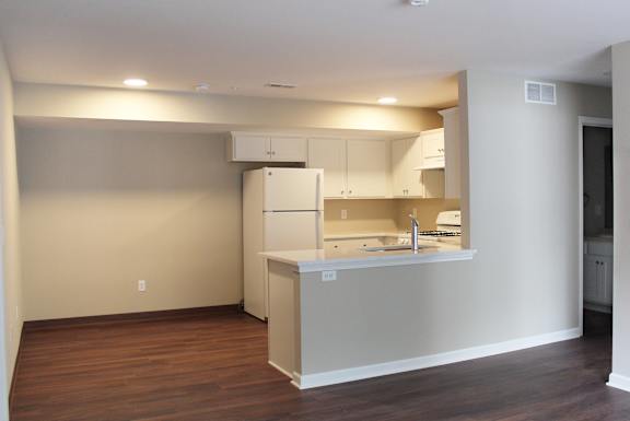an empty living room with a kitchen and a refrigerator