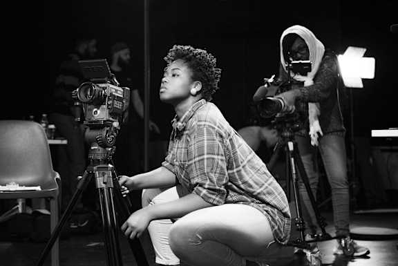 A person is sitting on a chair in front of a camera on a tripod.