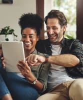 two people sitting on a couch looking at a tablet computer