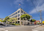 Thumbnail 2 of 25 - A large building with a flag on top is situated on a street corner.