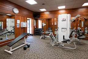 A gym with a variety of equipment including a weight bench, dumbbells, and a leg press machine.