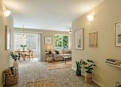 Thumbnail 1 of 8 - A living room with a couch, a table, a chair, a potted plant, and a framed picture on the wall.