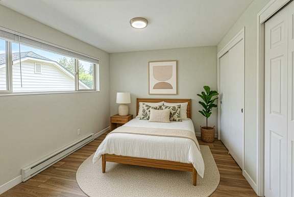 A bedroom with a bed, nightstand, and a plant.