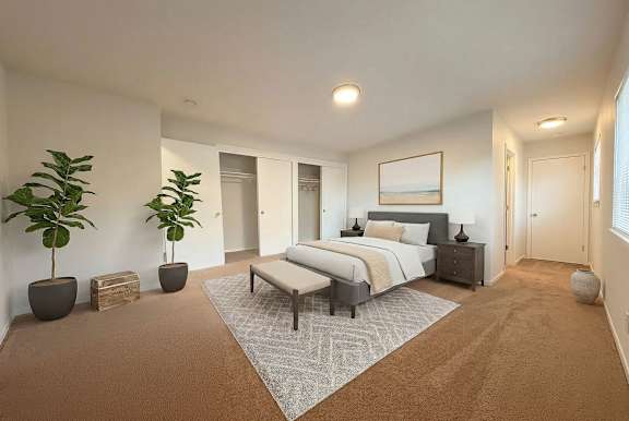 A bedroom with a large bed, a bench, and two potted plants.
