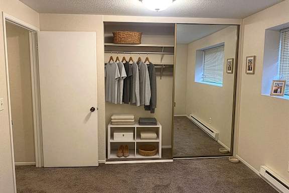 A white closet with clothes hanging up and a basket on the shelf.