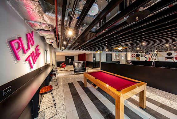 A pool table in a room with a neon sign that says "Play Time".