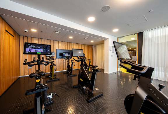 A gym with a row of exercise bikes and a television screen.