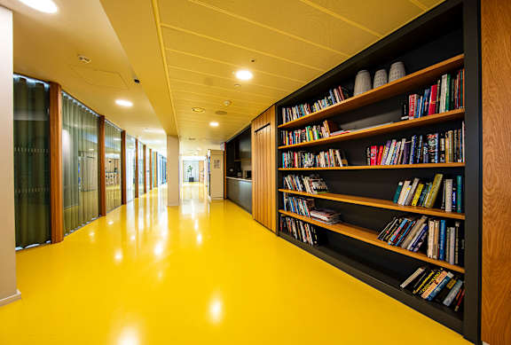 A long hallway with a yellow floor and a bookshelf on the right side.