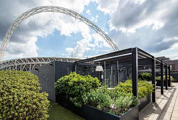 A modern building with a large arched structure in the background and a green planter in the foreground.