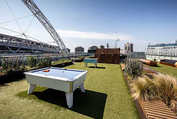 A pool table is set up on a grassy area with a stadium in the background.