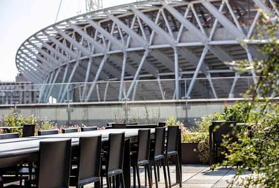 A large stadium with a unique design is in the background of a table and chairs.