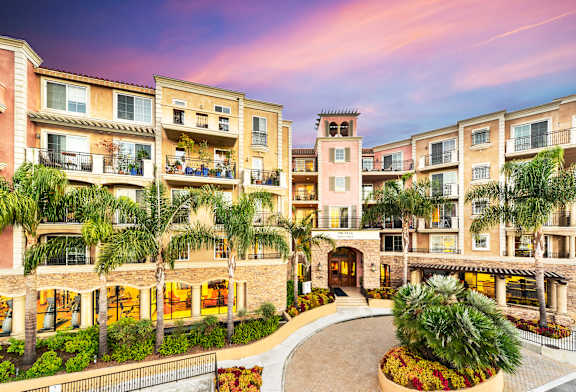 A sunset view of a multi-story residential building with balconies and palm trees.