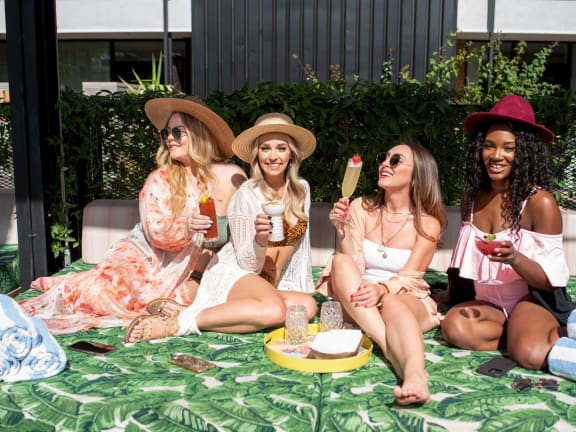 a group of women sitting on a blanket eating ice cream and drinking sangria