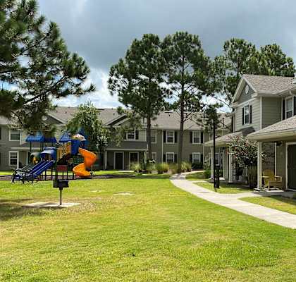 A playground with a slide is in the front yard of a house.