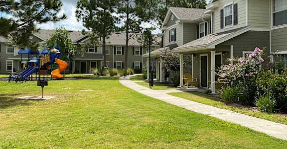 a large grassy area with a playground in front of a row of houses