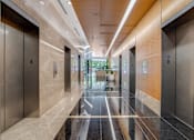 Thumbnail 12 of 15 - A long hallway with marble floors and elevators on either side.