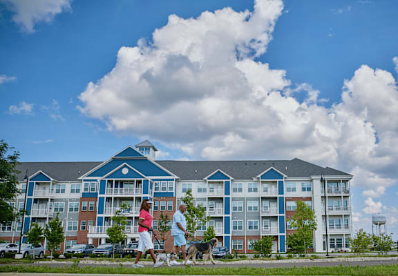 Two people walking a dog in front of a blue and red building.