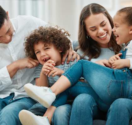 A family of four is sitting together on a couch, sharing a joyful moment.