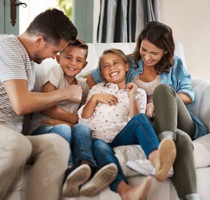 A family of four is sitting on a couch together.