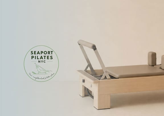 A wooden seaport pilates machine is on display with a logo in the corner.