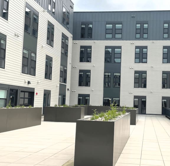A modern building with grey and white exterior and a courtyard with a planter.